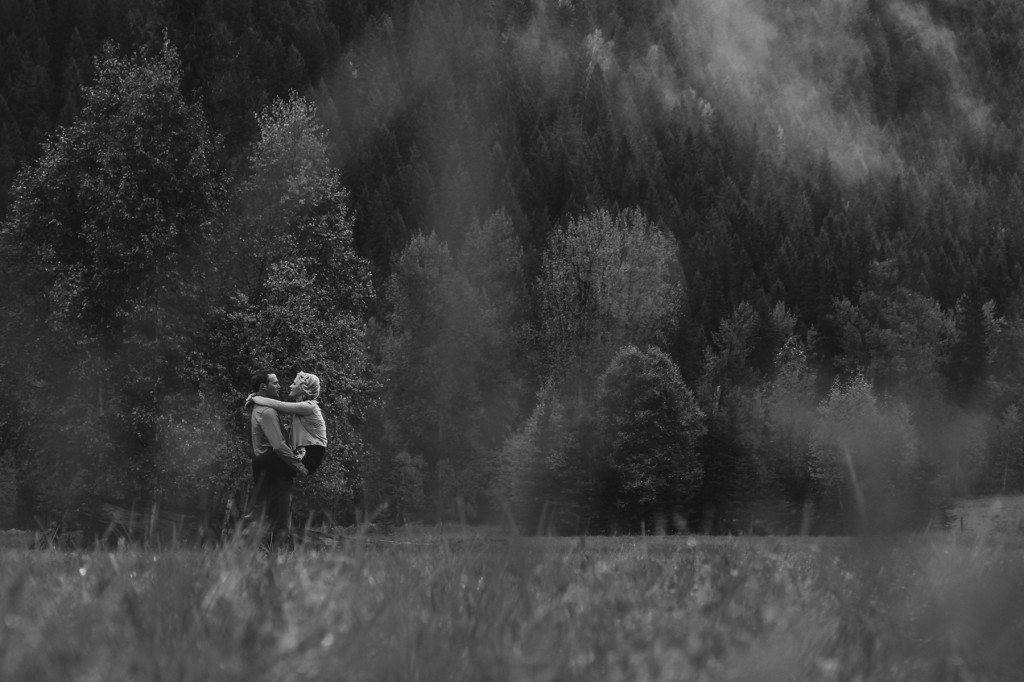 newly engaged woman straddles her fiance while he stands in a field in golden bc and they laugh