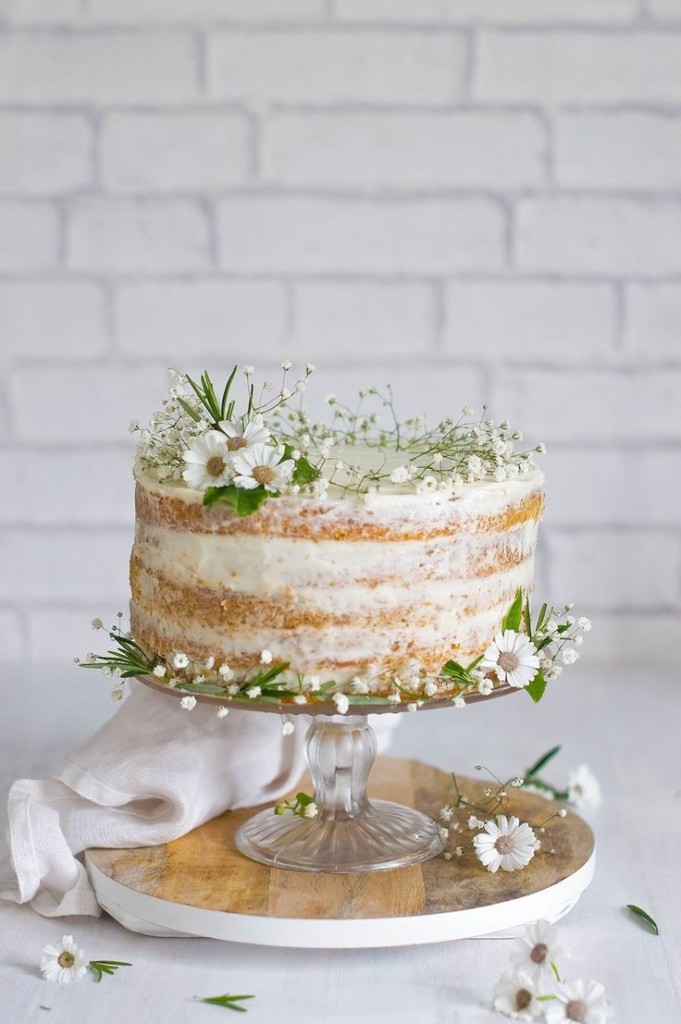 this naked cake sits on a pedestal with very little icing and some floral decorations on top of it