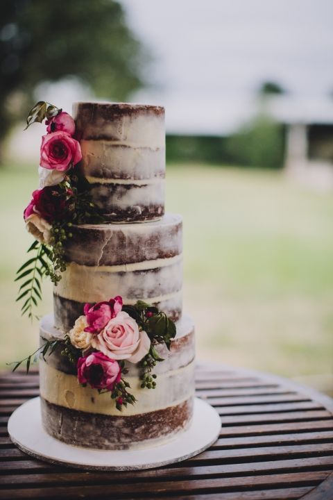 a stacked cake with no icing on the outside, only flowers to decorate it, sitting outside at a wedding in golden bc