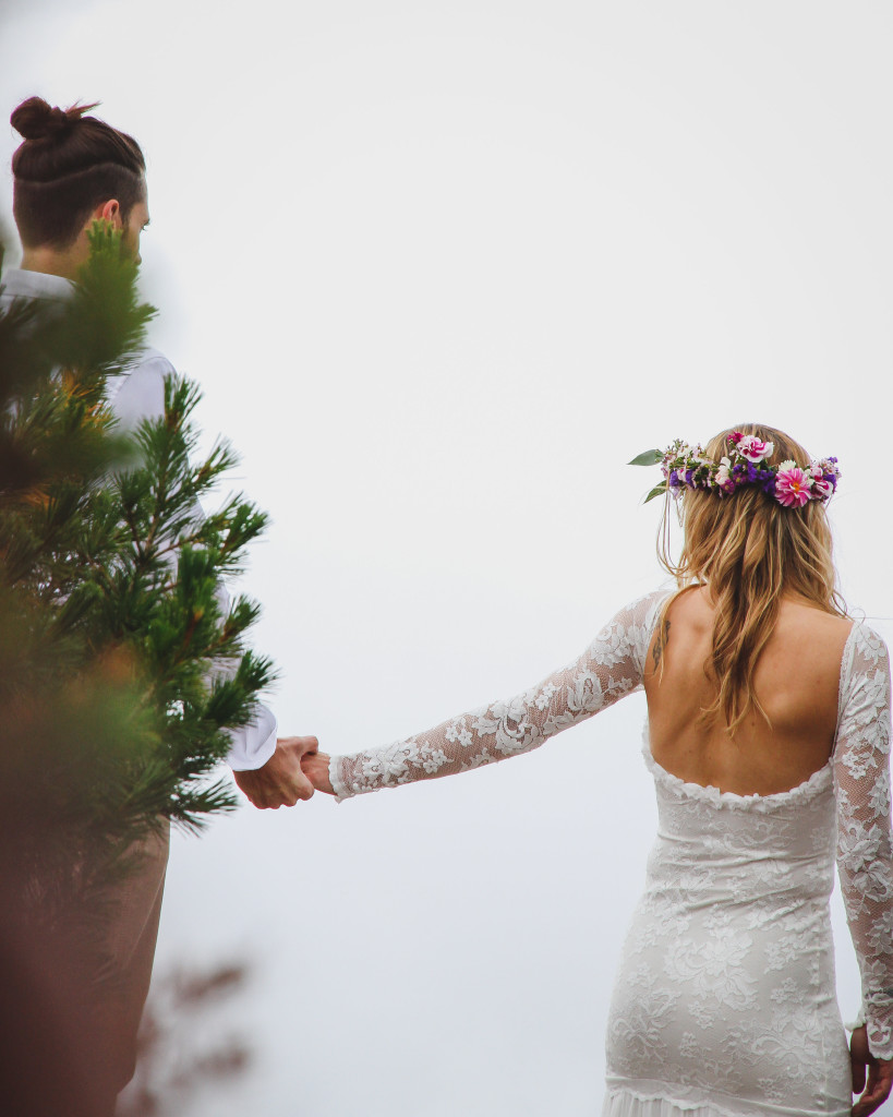 bride wearing floral crown wearing long sleeve wedding dress with lacey overlay on the arms holds her grooms hand 